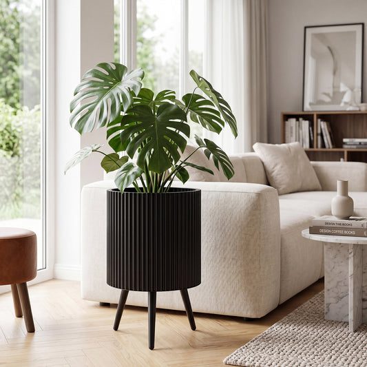 The black ribbed planter with a large green plant sits on a stand in a living room