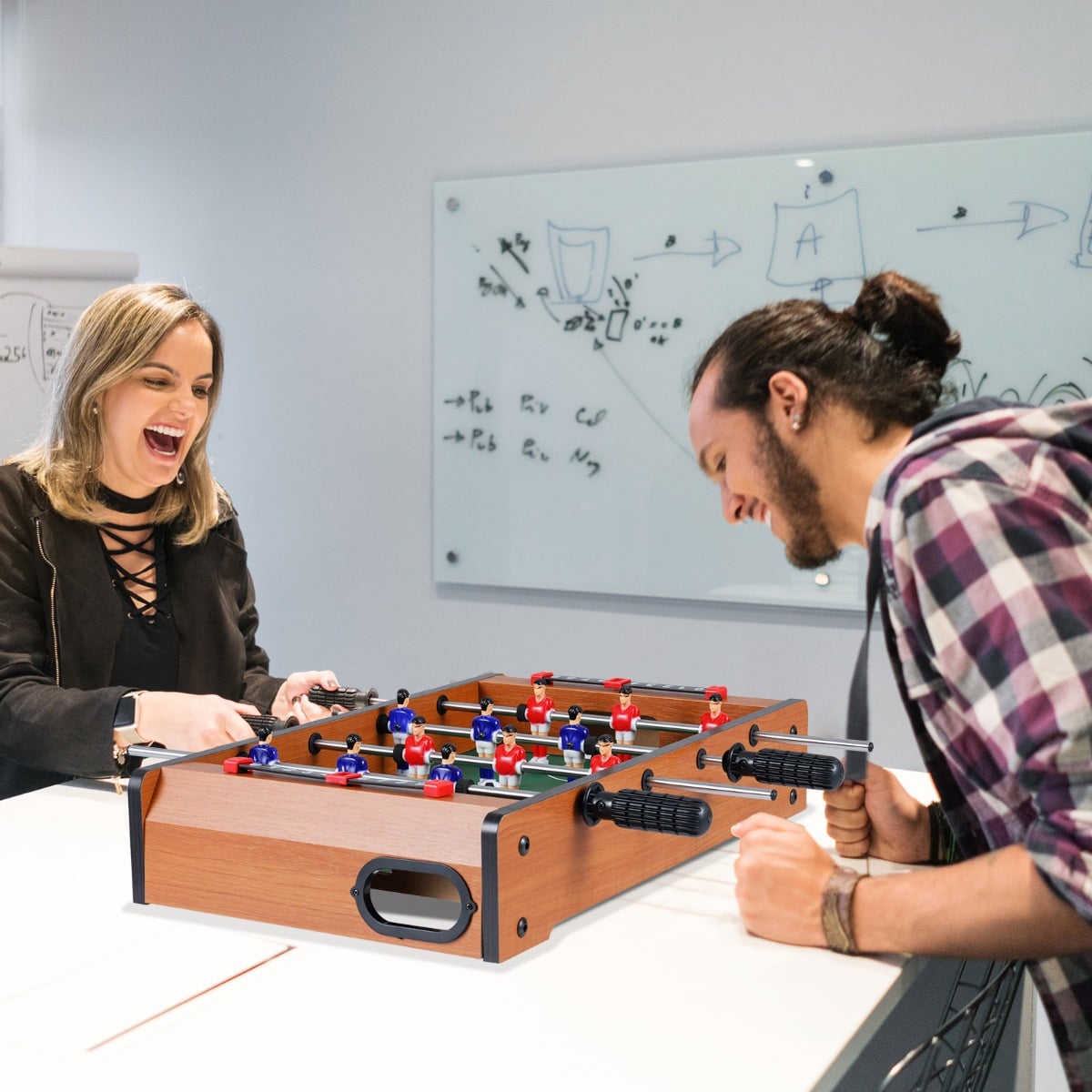 Two adults laughing while playing with the game room table in an office space