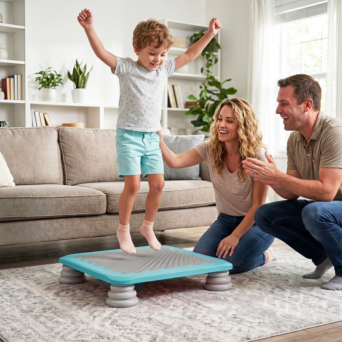 A happy family watches a young boy jump on the blue square trampoline in a living room