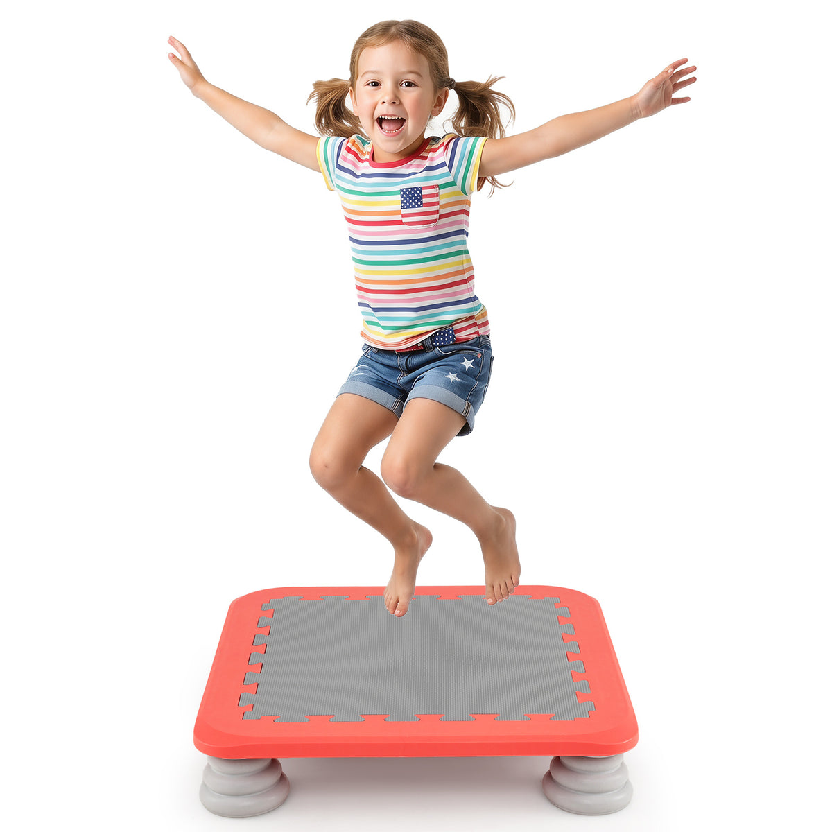 A joyful girl in a striped t-shirt jumps high on the red mini trampoline