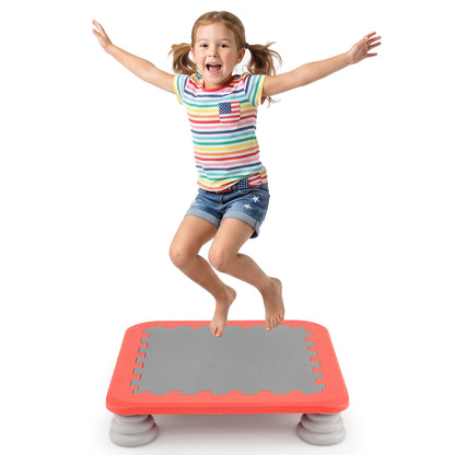 A joyful girl in a striped t-shirt jumps high on the red mini trampoline