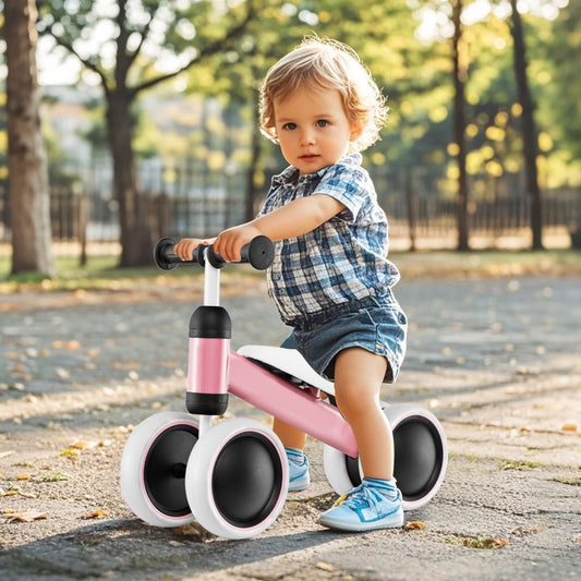 A toddler sits on the pink balance bike outdoors on a paved path