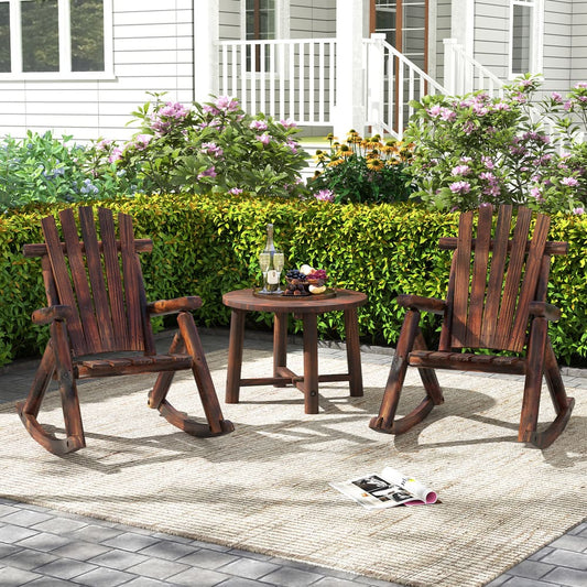 Two wooden Adirondack rocking chairs and a small table set up on a patio with a garden in the background