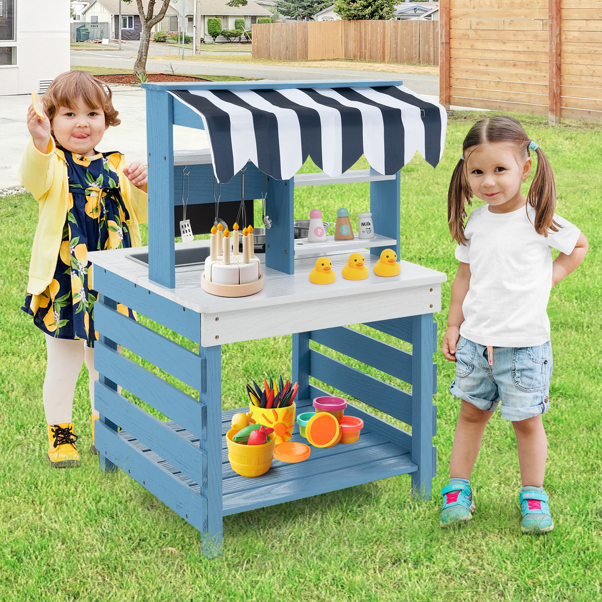 The play kitchen set being used by two children outdoors with toy food and ducks