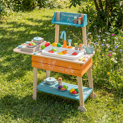 The wooden play kitchen set standing on a grassy lawn surrounded by colourful wildflowers
