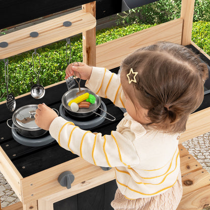 A young child playing with the play kitchen set using toy pots and food