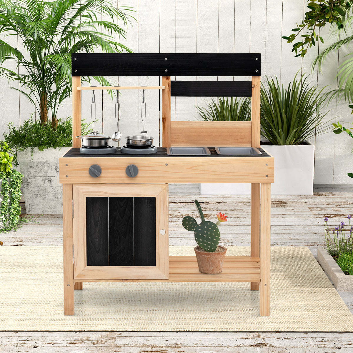 The play kitchen set standing on a patio rug surrounded by potted plants