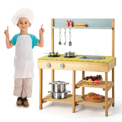 A young boy in a chef hat and apron pointing at the wooden play kitchen set