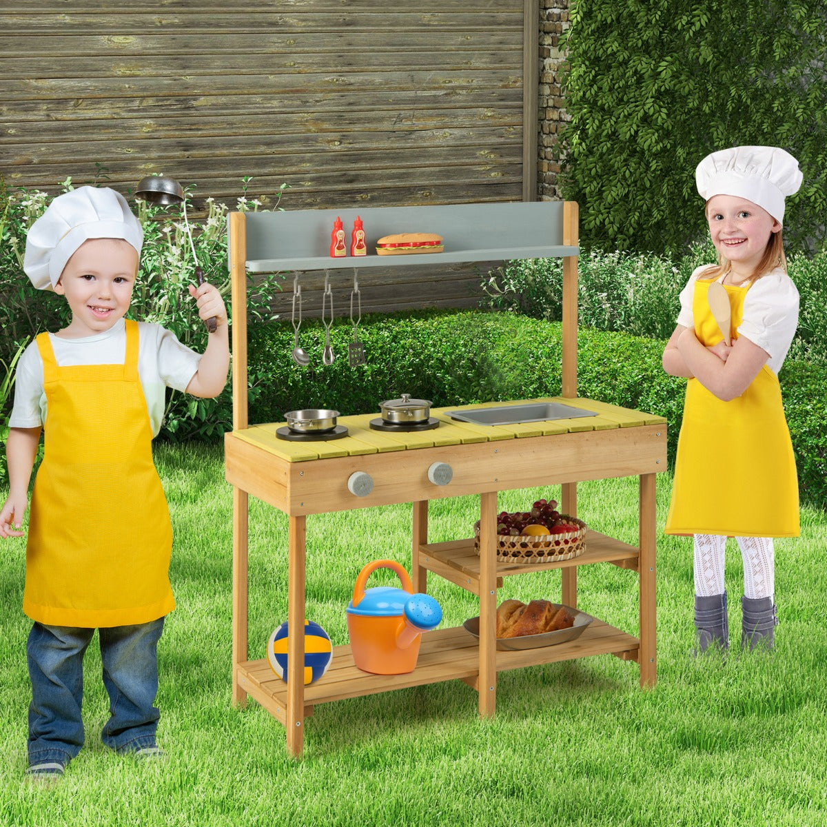 Two children in chef hats and aprons playing with the outdoor mud kitchen set in the garden