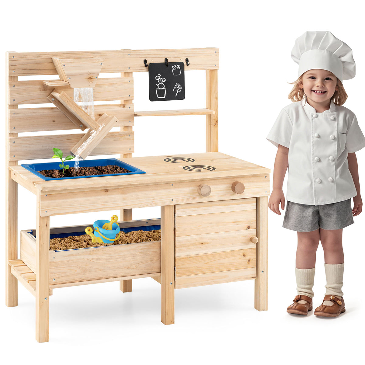 A child in a chef's hat and apron stands by the natural wood play kitchen