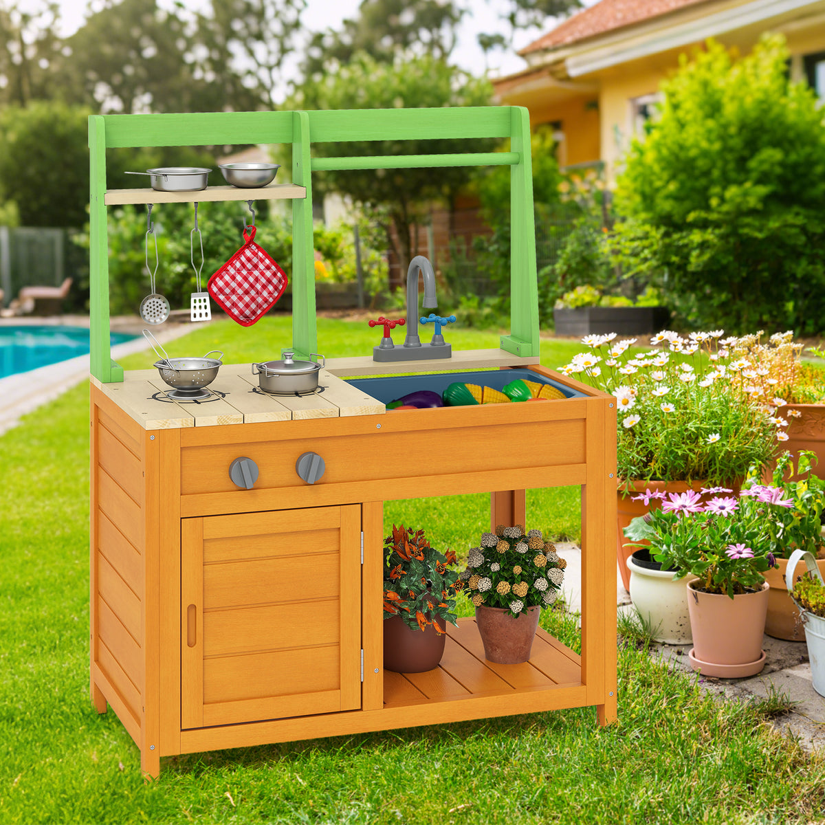 The outdoor play kitchen set in a garden setting next to a swimming pool, with plants and flowers around it
