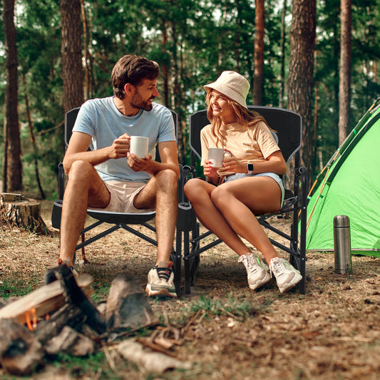 A man and woman sitting on the camping furniture in a forest setting near a tent