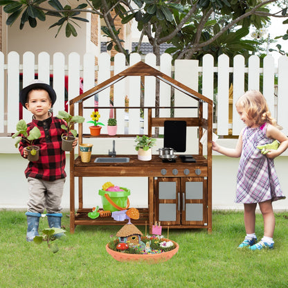 Two children interact with the wooden play kitchen set in a garden with a fence