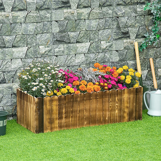 Wooden rectangular planter box filled with flowers, set on grass with a stone wall behind