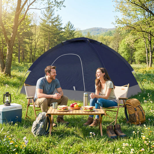 A couple enjoying a picnic outside a navy blue two person camping tent in a sunny meadow