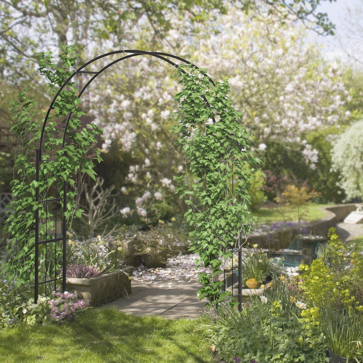 A black metal garden arch trellis covered in green climbing plants in a garden setting
