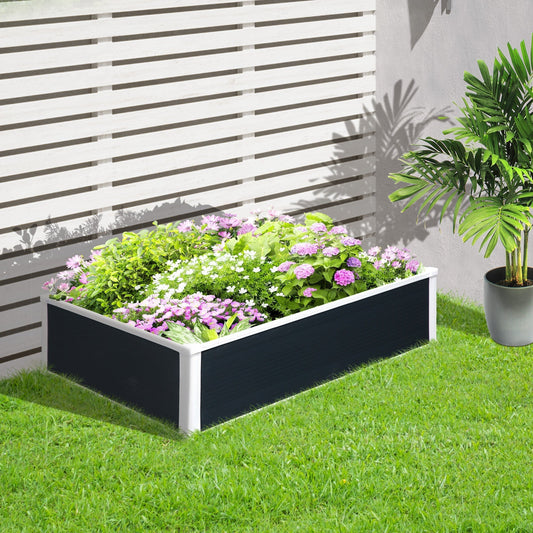 The planter box placed on a green lawn in a garden setting with various colourful plants