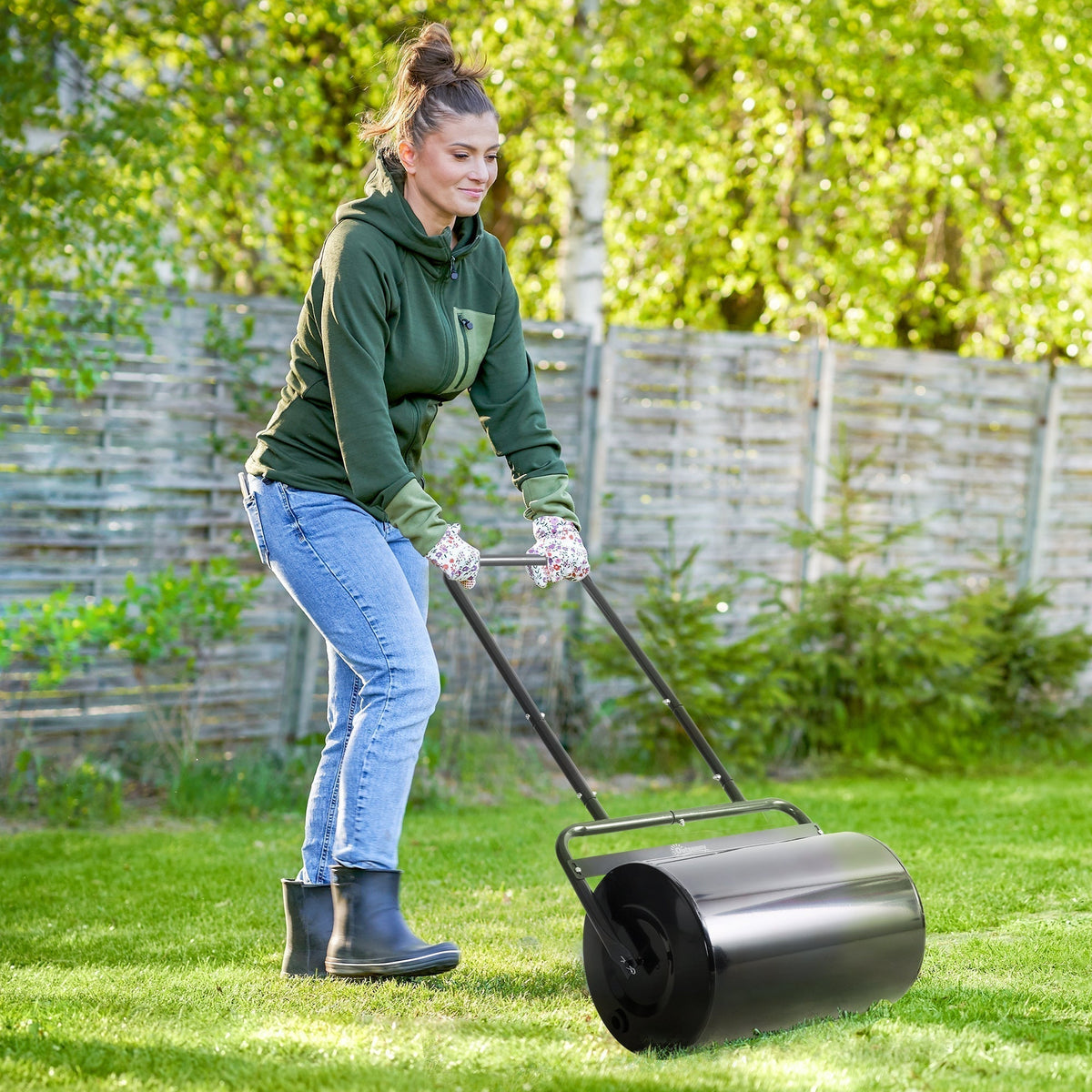 Woman using the fillable cylinder steel lawn roller on a green lawn in a garden