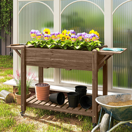 Wooden raised planter filled with colourful pansies, pots and gardening tools nearby