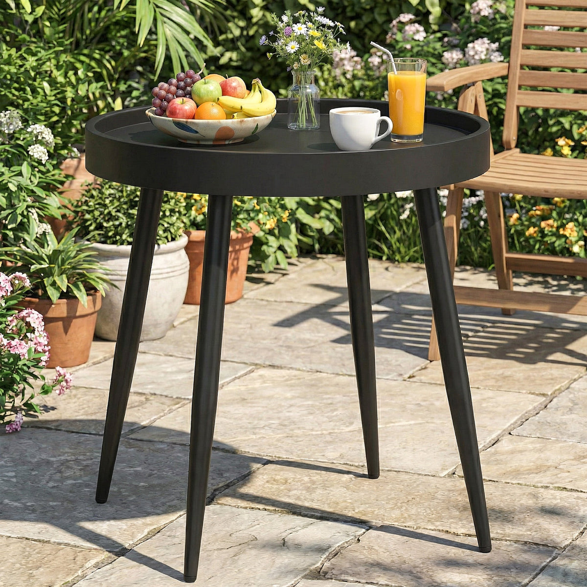 A black round garden table with a fruit bowl and drinks on it, placed on a patio