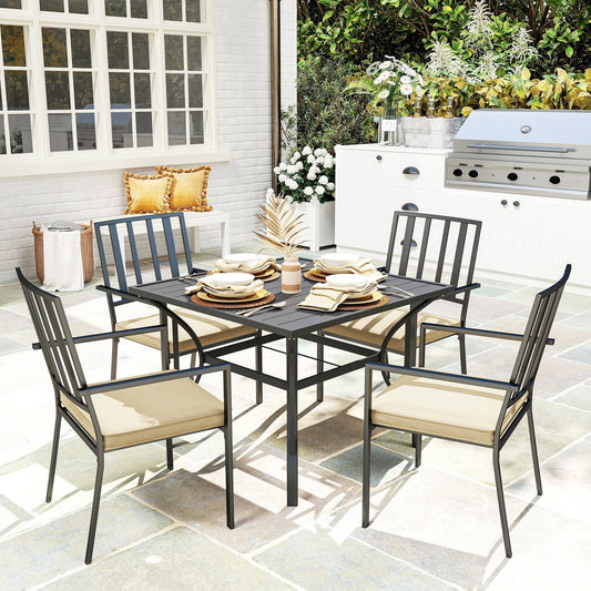 A black metal garden dining set with four chairs and a table, set up on a patio with outdoor kitchen in background