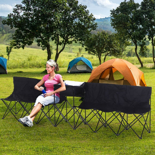A woman sits on the portable sports team bench in a grassy field with tents behind her