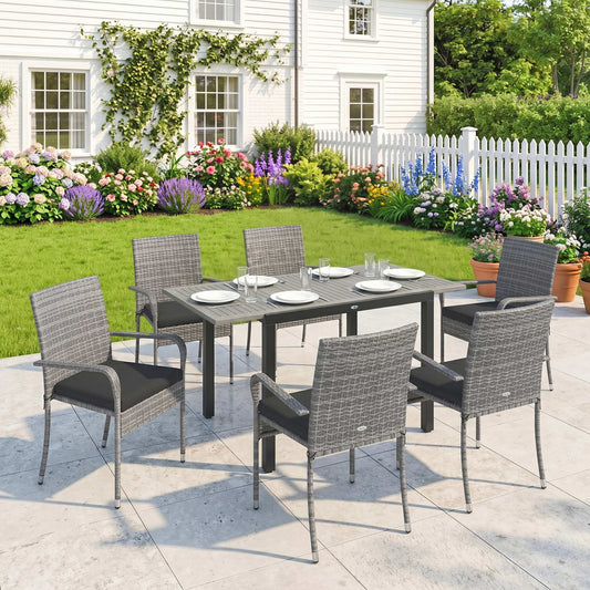 the rattan furniture set arranged on a patio in front of a white house with a garden