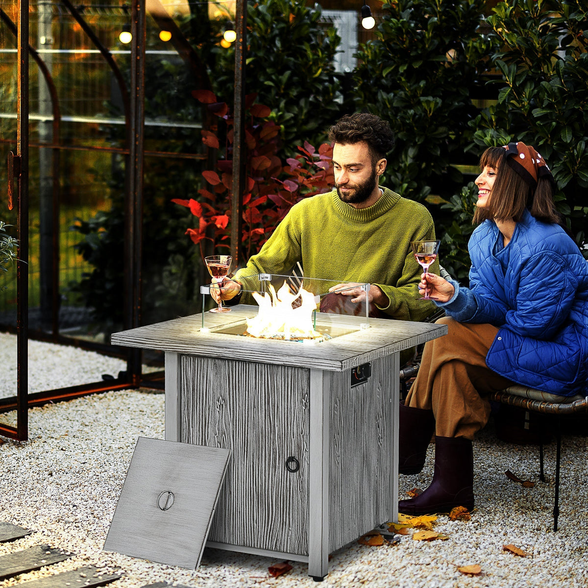 A couple enjoying the gas fire pit table in a garden setting with drinks