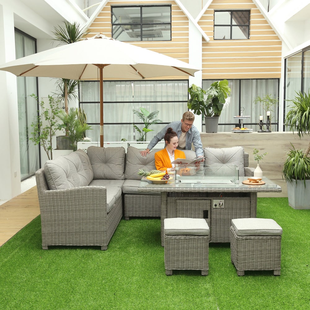 A couple relaxing on the grey rattan corner sofa with fire pit table and footstools in a modern garden setting