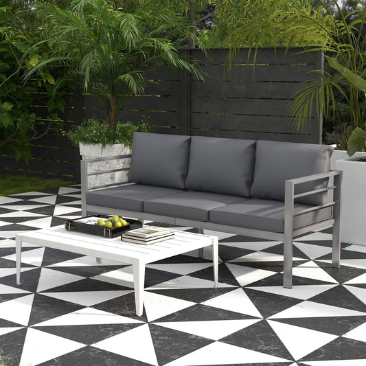 A grey three-seater garden bench with cushions placed on a patio next to a white coffee table
