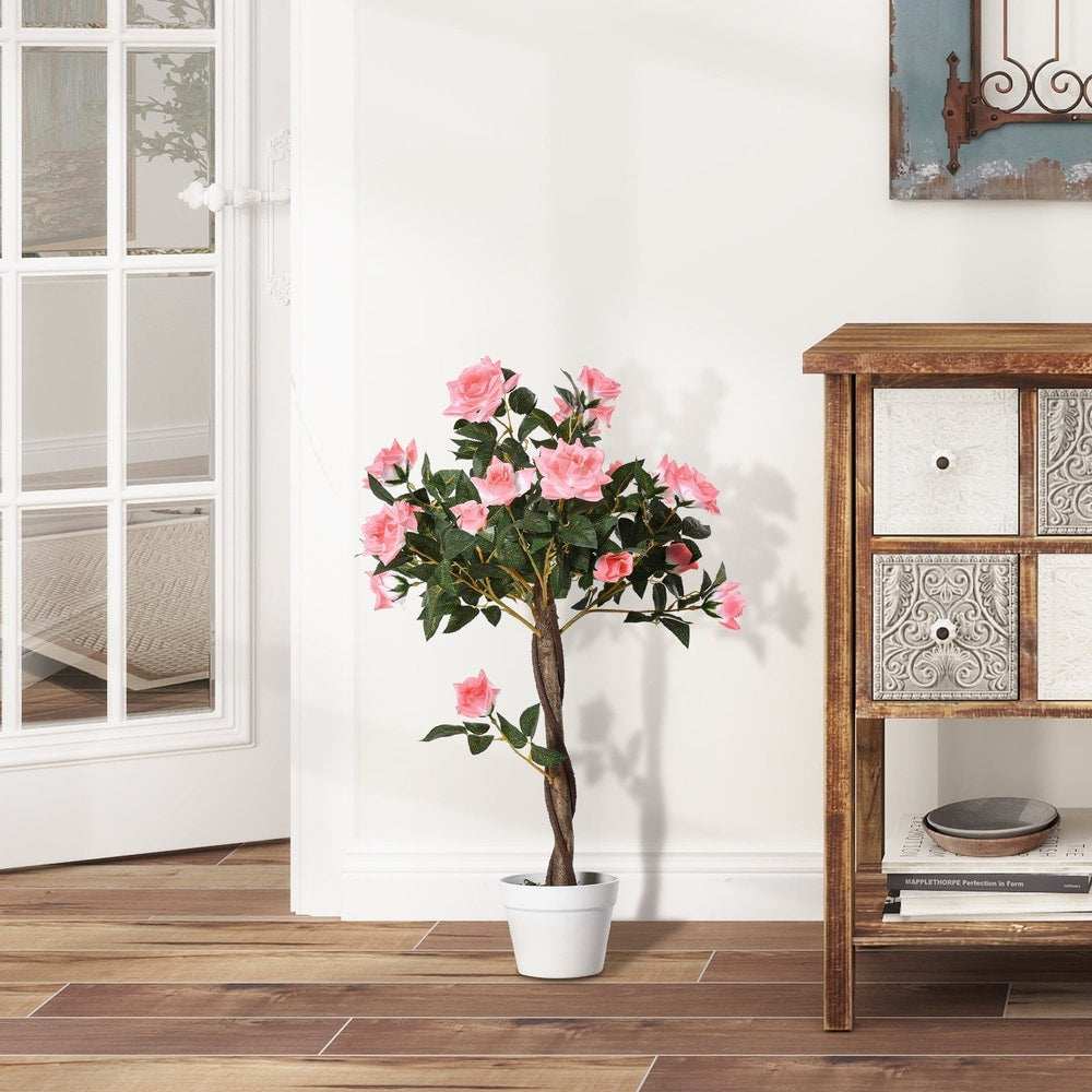 The artificial pink rose floral plant sits on a wooden floor next to a wooden cabinet and a white door