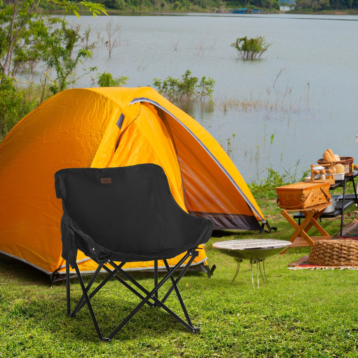 The black camping chair set up outside a tent by a lake, with a small barbecue and picnic basket