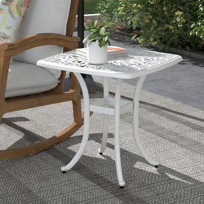 The white square garden table placed on a patio next to a rocking chair, with a plant on top