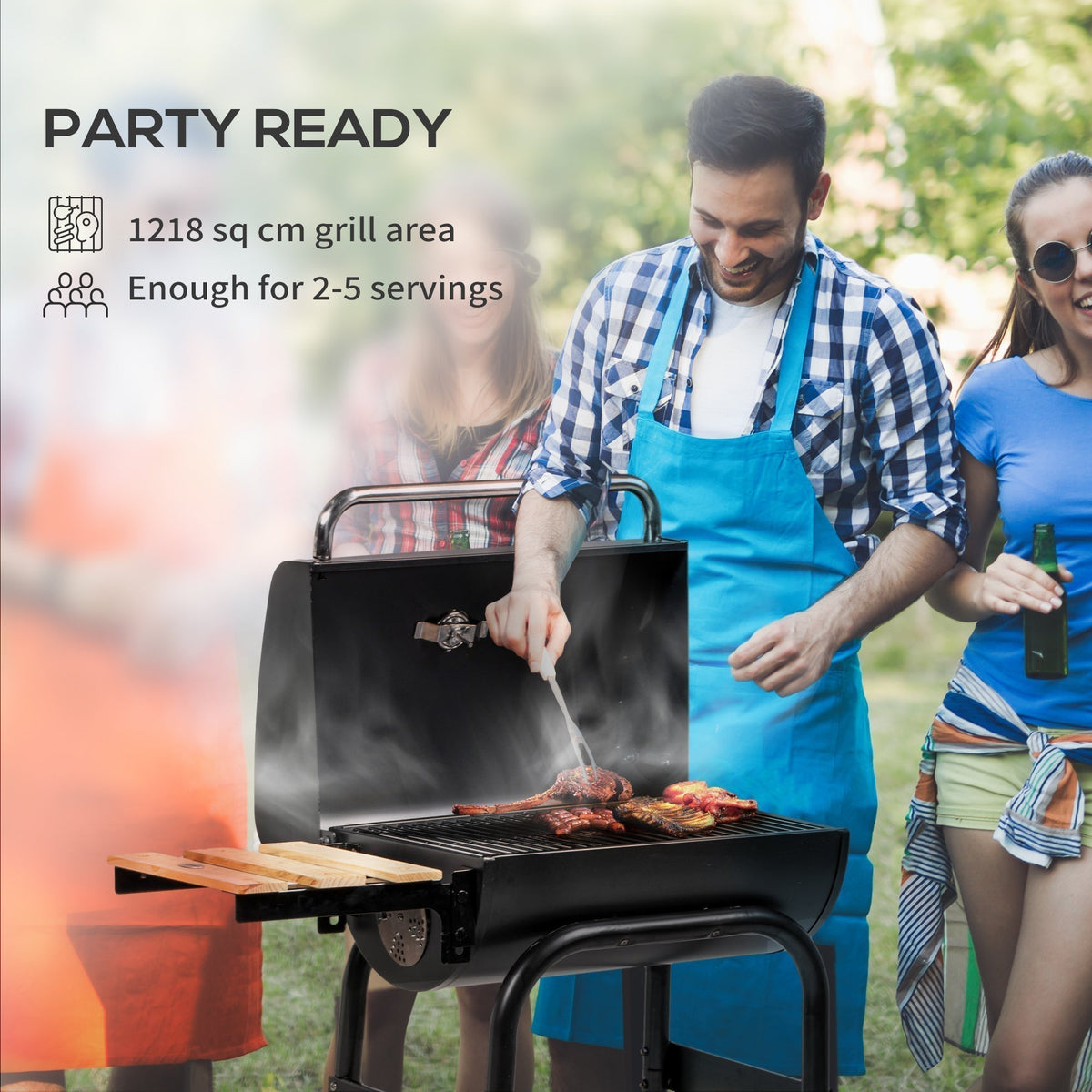 The charcoal grill being used by a man in an apron at an outdoor party with friends