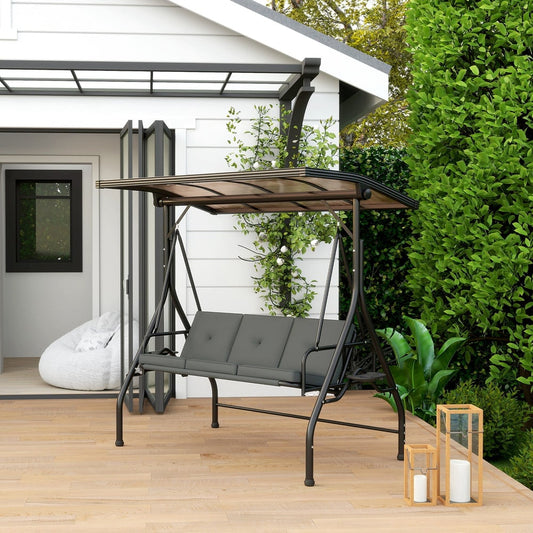 Dark grey three-seater swing bench bed with canopy on a wooden deck next to green foliage