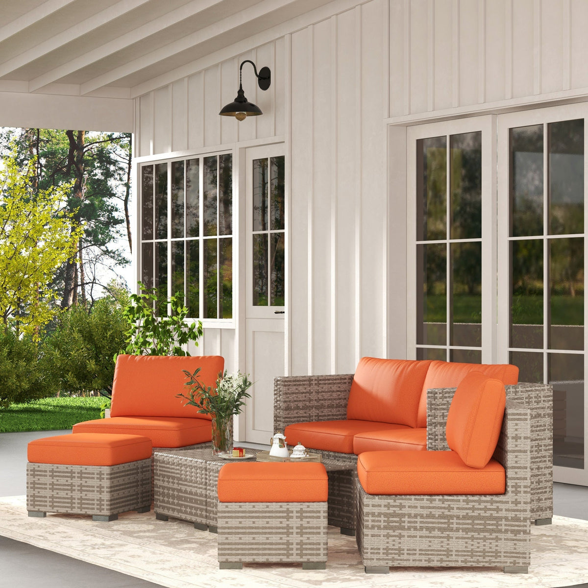 The rattan garden set with orange cushions placed on a patio next to a house