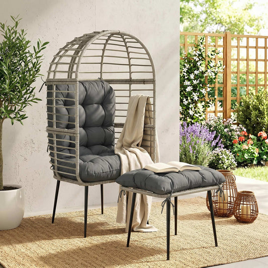 The rattan egg chair with footstool set placed on a rug in a garden setting with plants and flowers
