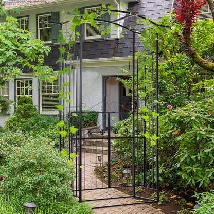 The garden arch standing on a brick path in front of a house entrance with climbing plants