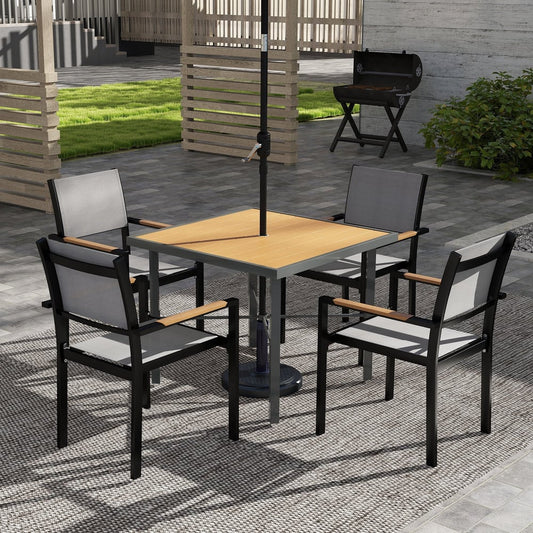 Four chairs around a square outdoor dining table set up on a patio with a barbecue in the background