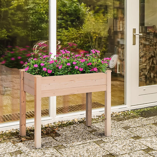 A rectangular raised planter with plants growing in it, placed on a patio next to a glass door