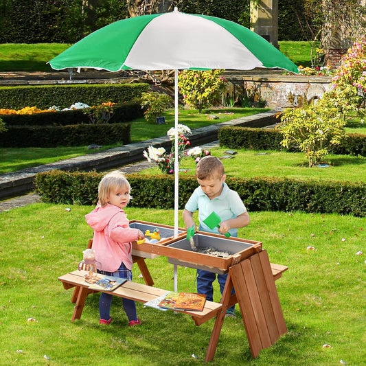 Two children playing at the wooden sand and water table with benches and parasol in a garden setting