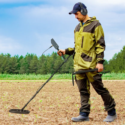 The metal detector being used by a person wearing headphones while walking across a field