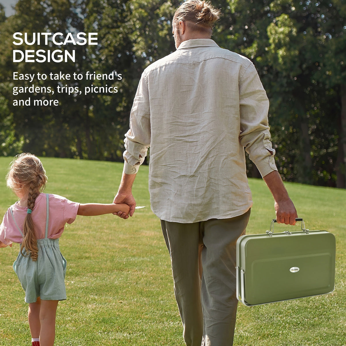 A man and child walking in a park holding the green portable charcoal grill, highlighting its suitcase design