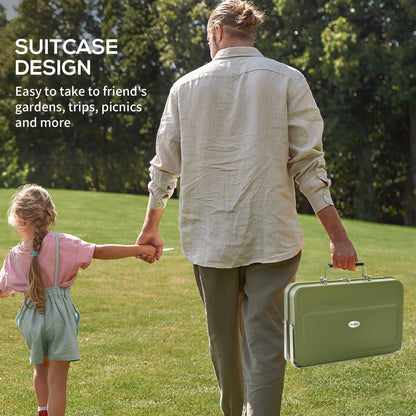 A man and child walking in a park holding the green portable charcoal grill, highlighting its suitcase design