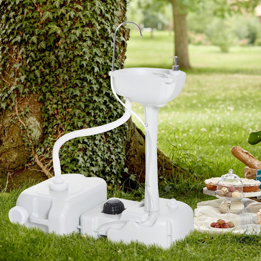 The portable camping sink is set up outdoors on grass with a picnic spread nearby