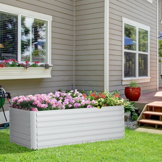A galvanised raised garden bed filled with flowers, placed on a lawn next to a house patio