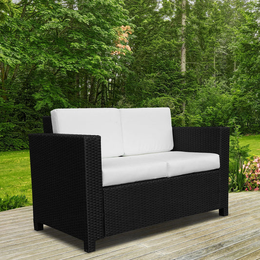 The black rattan garden loveseat sits on a wooden deck with green trees behind