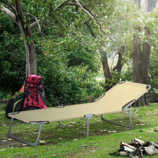 The beige camping bed set up on grass with backpacks and logs nearby