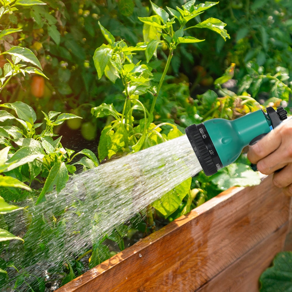 A hand holding the spray nozzle of the hose reel, watering green plants