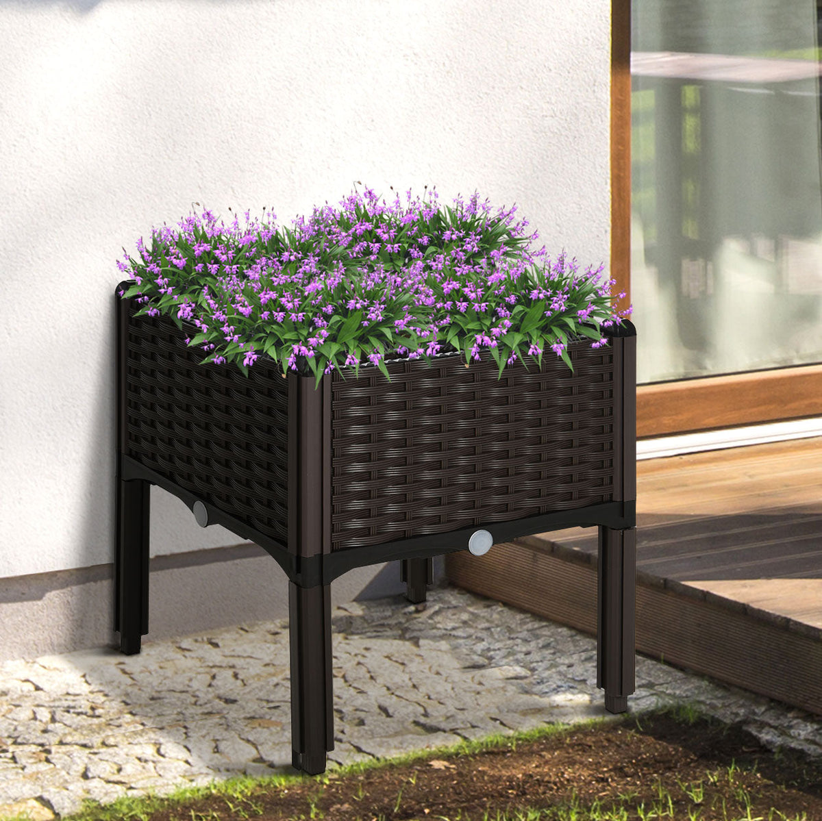 The elevated planter box filled with purple flowers placed on a patio next to a house wall